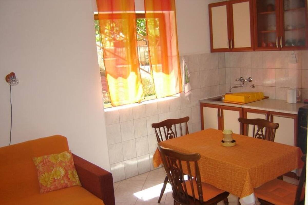 A dining area with a table and chairs, a kitchen with cabinets, and a window with curtains.