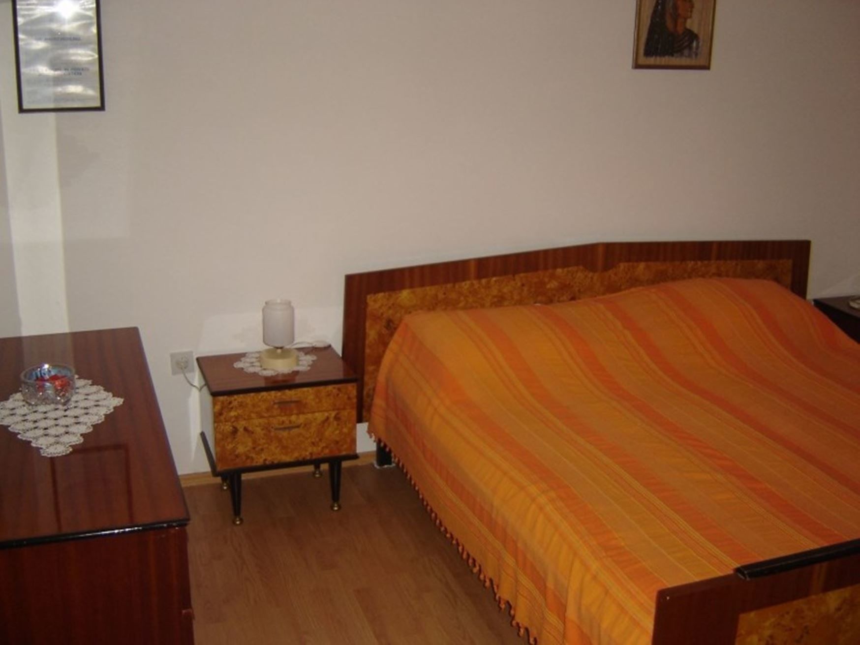 A bedroom with a wooden bed, a nightstand, a dresser, and a framed picture on the wall.