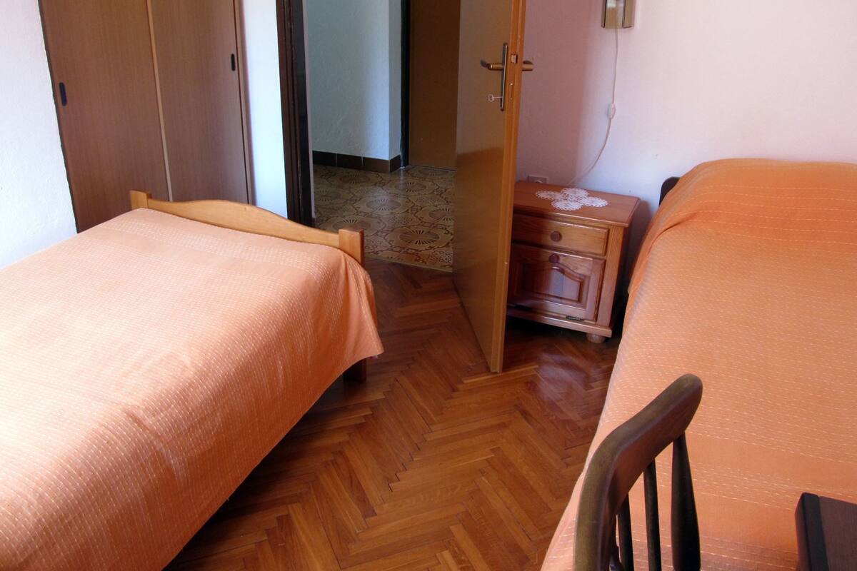 A bedroom with two single beds, wooden flooring, a nightstand, and a wardrobe.