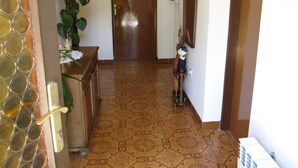 A hallway with patterned floor tiles, a wooden door, a potted plant, and a small table with a vase. - Apartment Grgorinic (Pula)