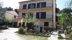 A two-story building with a stone entrance, a small garden, and a paved driveway. - Apartment Grgorinic (Pula)