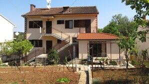 A two-story house with a tiled roof, a balcony, and a garden area with plants and a hose. - Apartment Grgorinic (Pula)