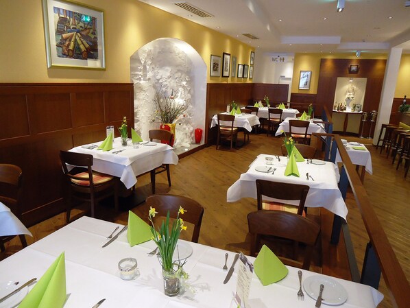 Un restaurante con varias mesas dispuestas para comer, con servilletas verdes, cubiertos y centros de mesa florales.
