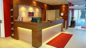 A modern reception desk with a wooden finish, a red carpet, and a glass door leading outside. - Hotel Gasthof Posthalter (Zwiesel)