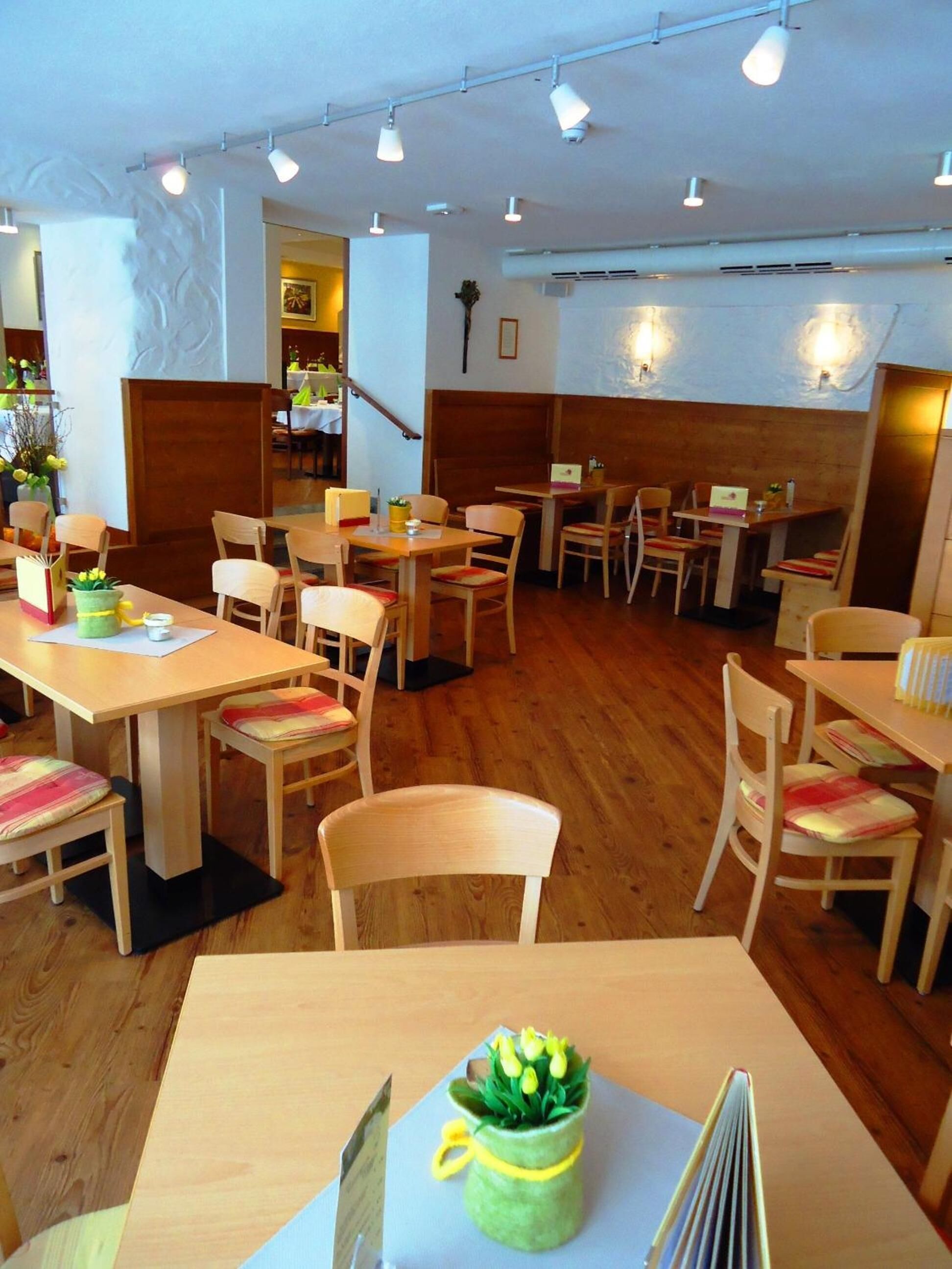 Un interior de restaurante acogedor, con mesas y sillas de madera, una escalera y una iluminación decorativa en las paredes.