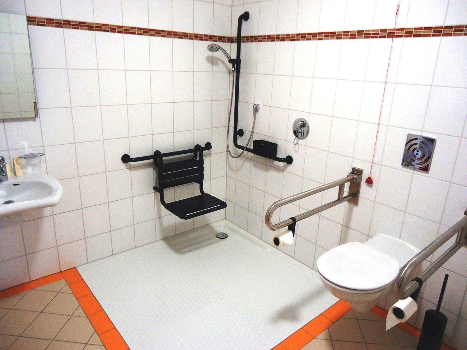 A bathroom with a white sink, a toilet, a shower with a grab bar, and a towel rack.