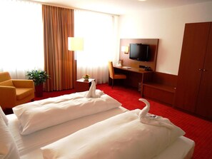 A hotel room with two beds, a desk, a television, a chair, and a potted plant. - Hotel Gasthof Posthalter (Zwiesel)