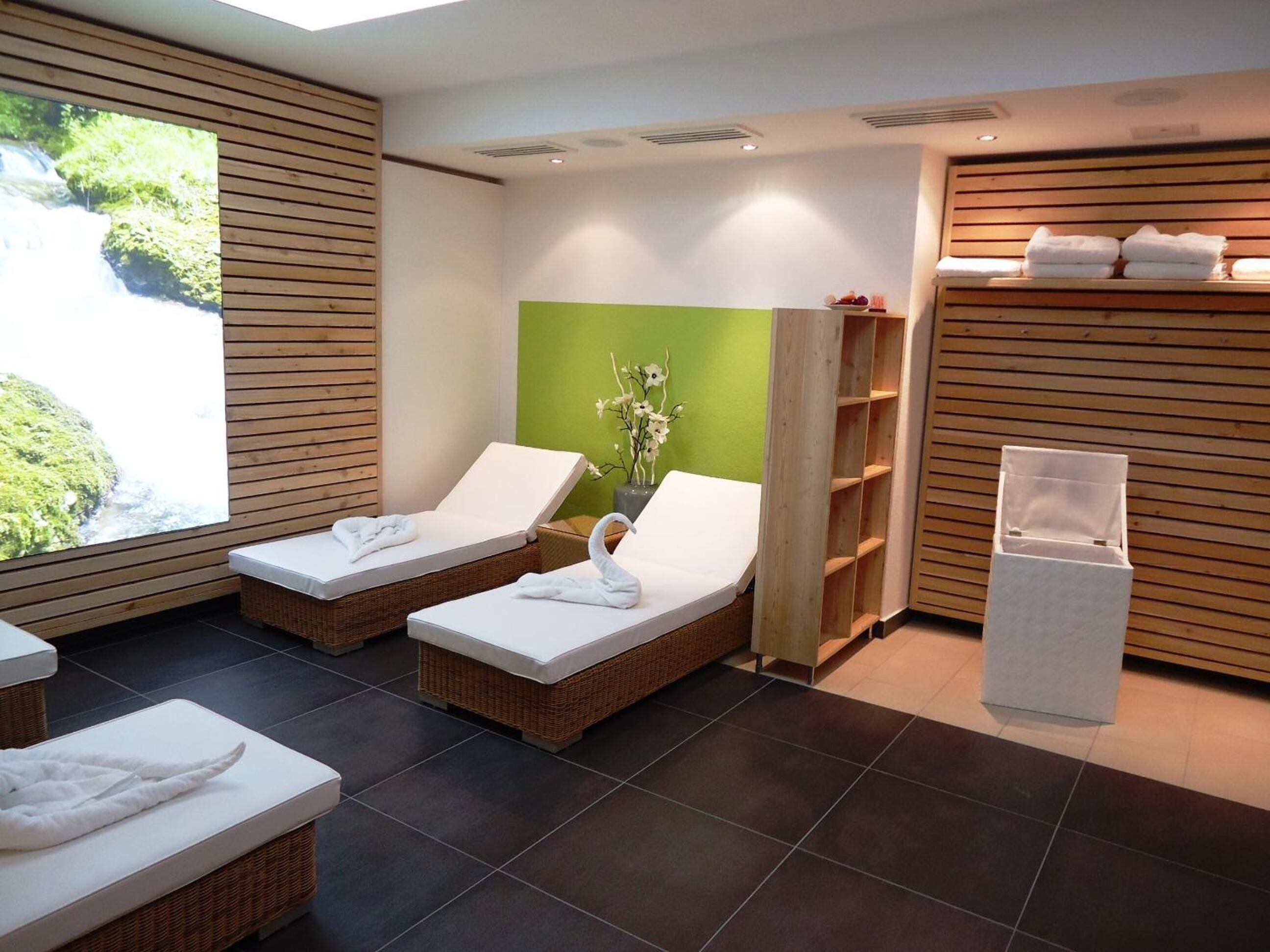 Ein Spa-Raum mit zwei Liegestühlen, einer grünen Wand und einem Holzregal mit Handtüchern.