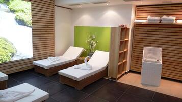 Ein Spa-Raum mit zwei Liegestühlen, einer grünen Wand und einem Holzregal mit Handtüchern.