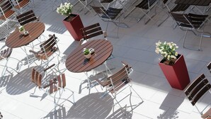 An outdoor seating area with round tables and chairs, surrounded by potted plants. - Hotel Gasthof Posthalter (Zwiesel)