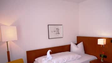 Una habitación de hotel con una cama, una silla, una mesita de noche con lámpara y un cuadro en la pared.