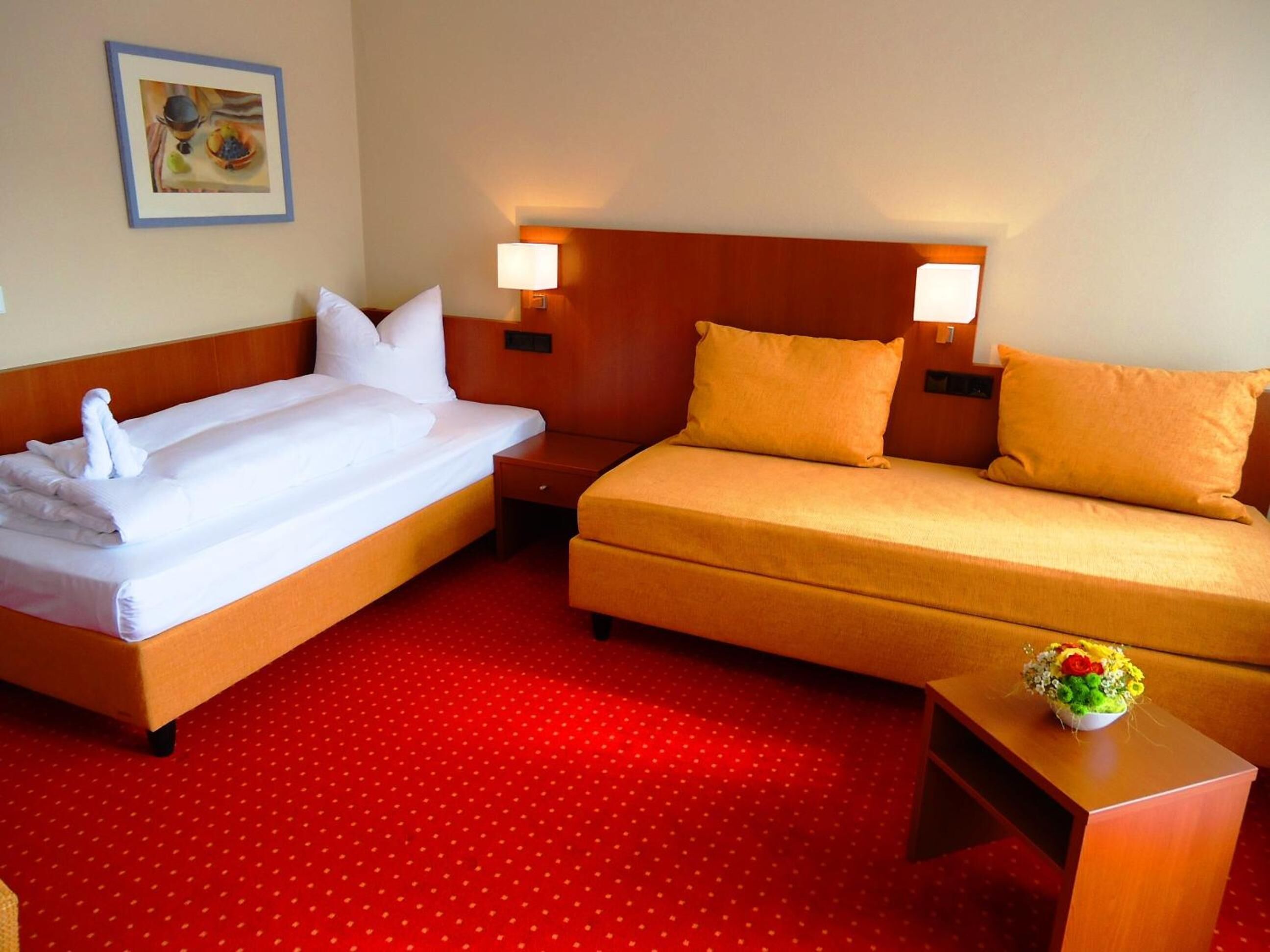 A hotel room with two beds, a red polka dot carpet, a nightstand with a vase of flowers, and a painting on the wall.