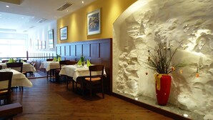 A restaurant interior with wooden flooring, tables with white tablecloths, and a decorative wall with a red vase. - Hotel Gasthof Posthalter (Zwiesel)