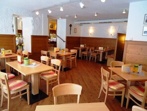 A restaurant with wooden tables and chairs, a staircase, and a wall-mounted light fixture. - Hotel Gasthof Posthalter (Zwiesel)