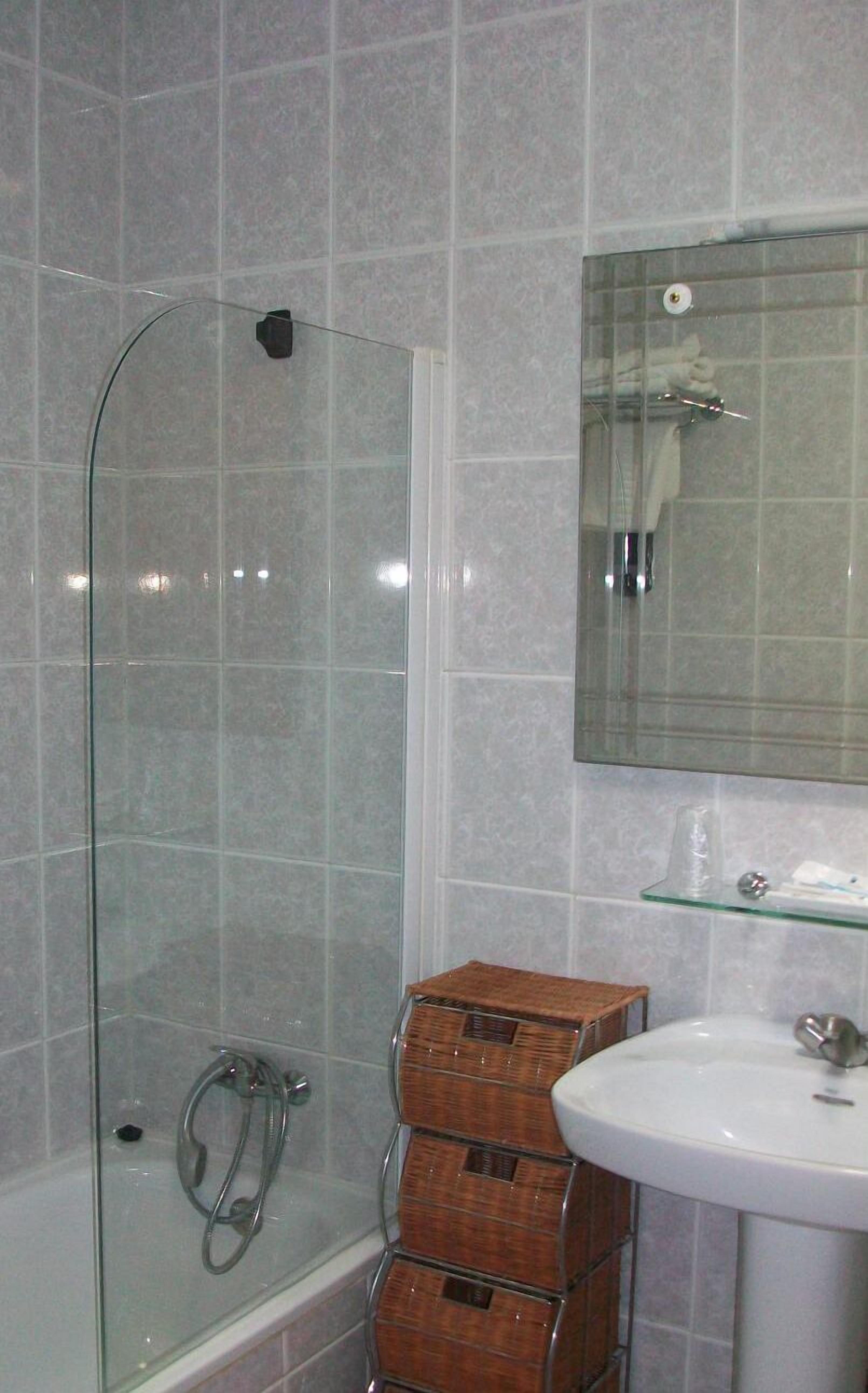 A bathroom with a glass shower enclosure, a white sink, and a mirror above it.
