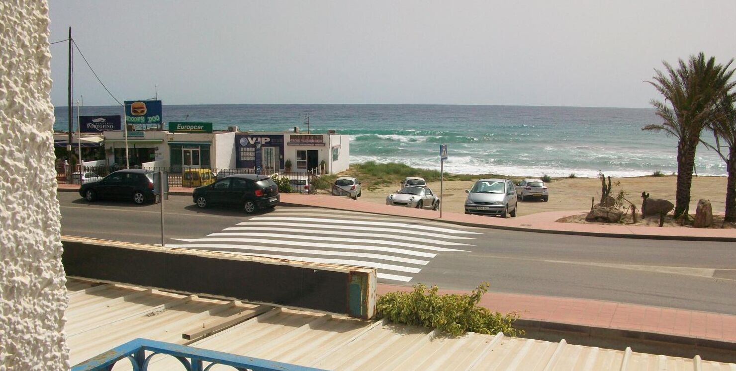 A coastal road with cars parked along the side, a pedestrian crossing, and a view of the ocean.