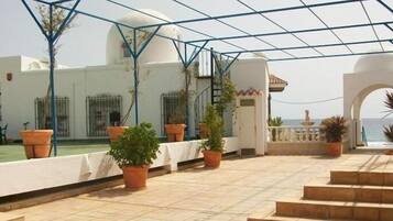 Un espacio al aire libre cubierto con plantas en macetas, un edificio blanco con cúpula y vista al mar.