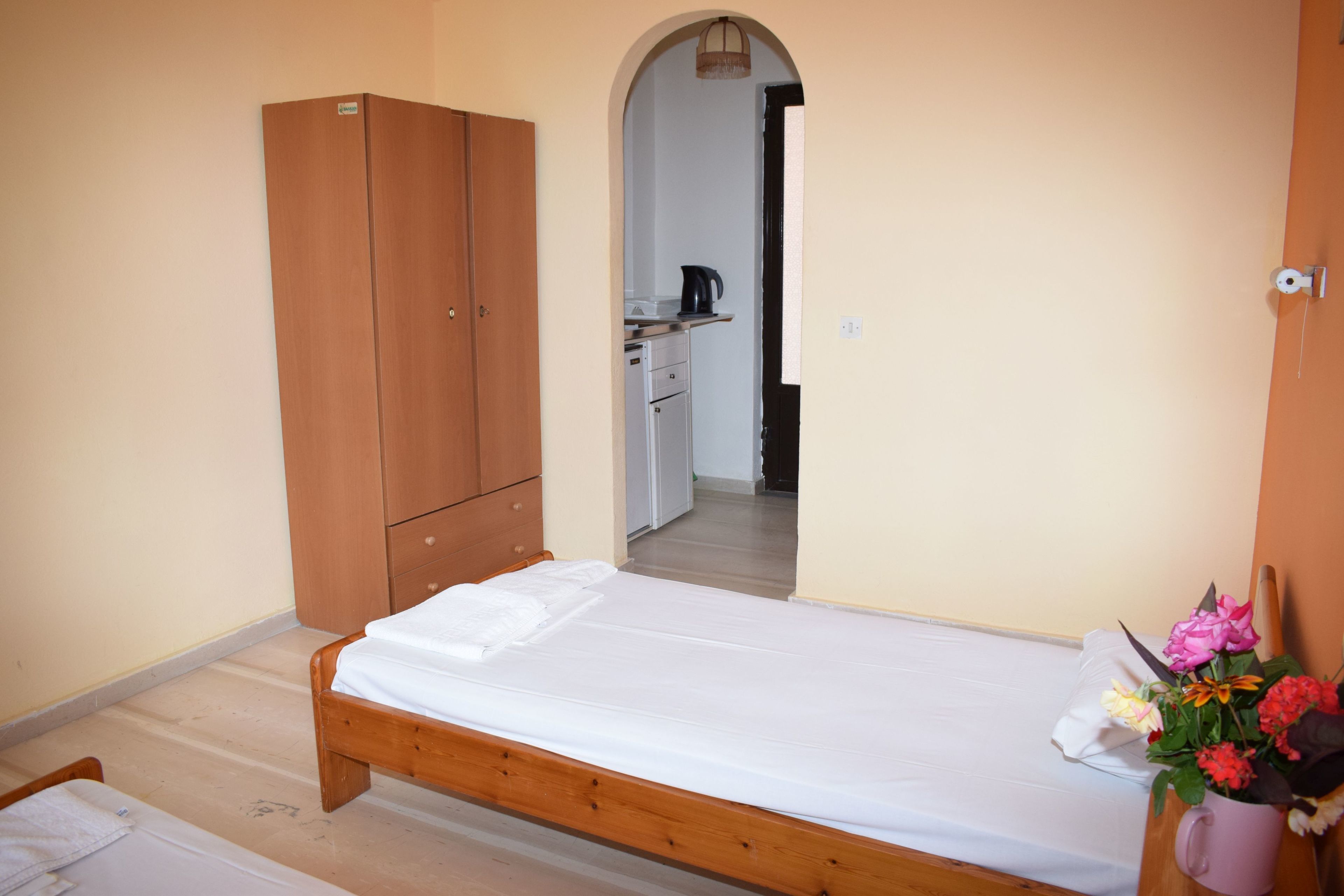 Une chambre avec un lit en bois, une armoire et, au fond, un coin cuisine.