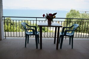 A balcony with two chairs and a table, overlooking a scenic view of the sea and distant mountains.