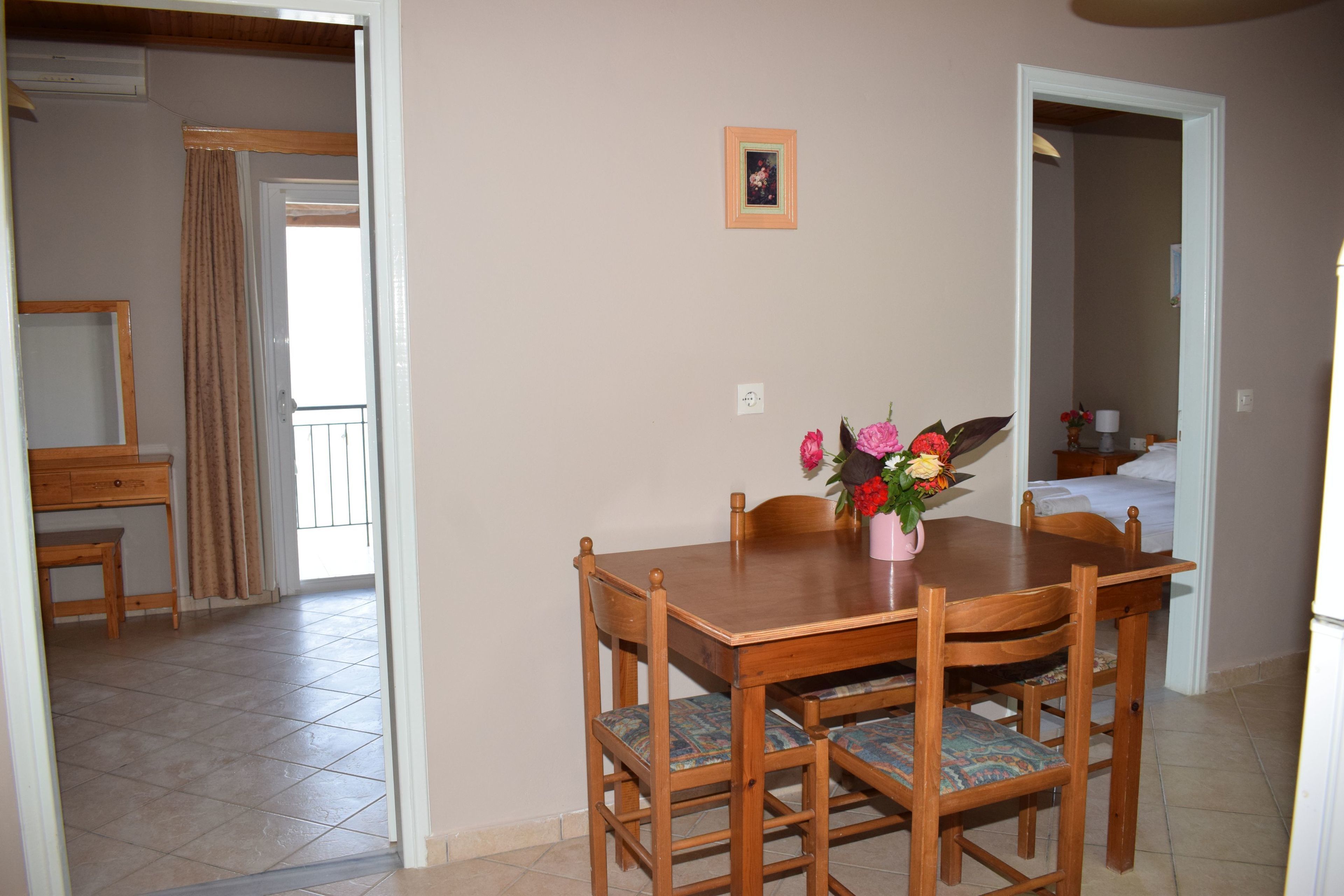 A dining area with a wooden table and chairs, a vase with flowers, and a small framed picture on the wall.