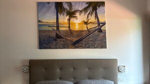 A bedroom with a bed, a headboard, and a wall-mounted painting of a beach scene. - Hotel Villa Mare (Posada)