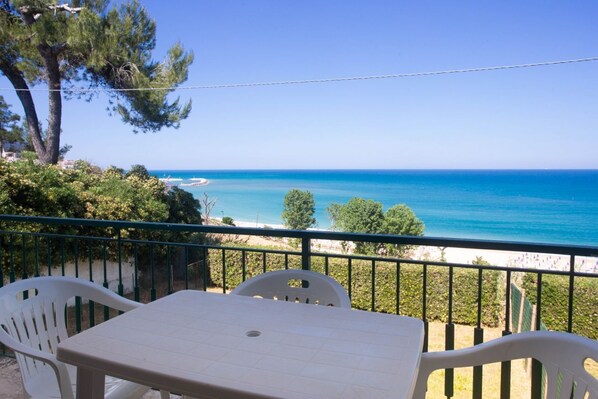 A balcony with a table and chairs overlooking a beach.