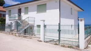 Un edificio di due piani con un balcone, una scala e un ingresso chiuso da cancello.
