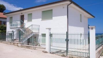 Un edificio di due piani con un balcone, una scala e un ingresso chiuso da cancello.