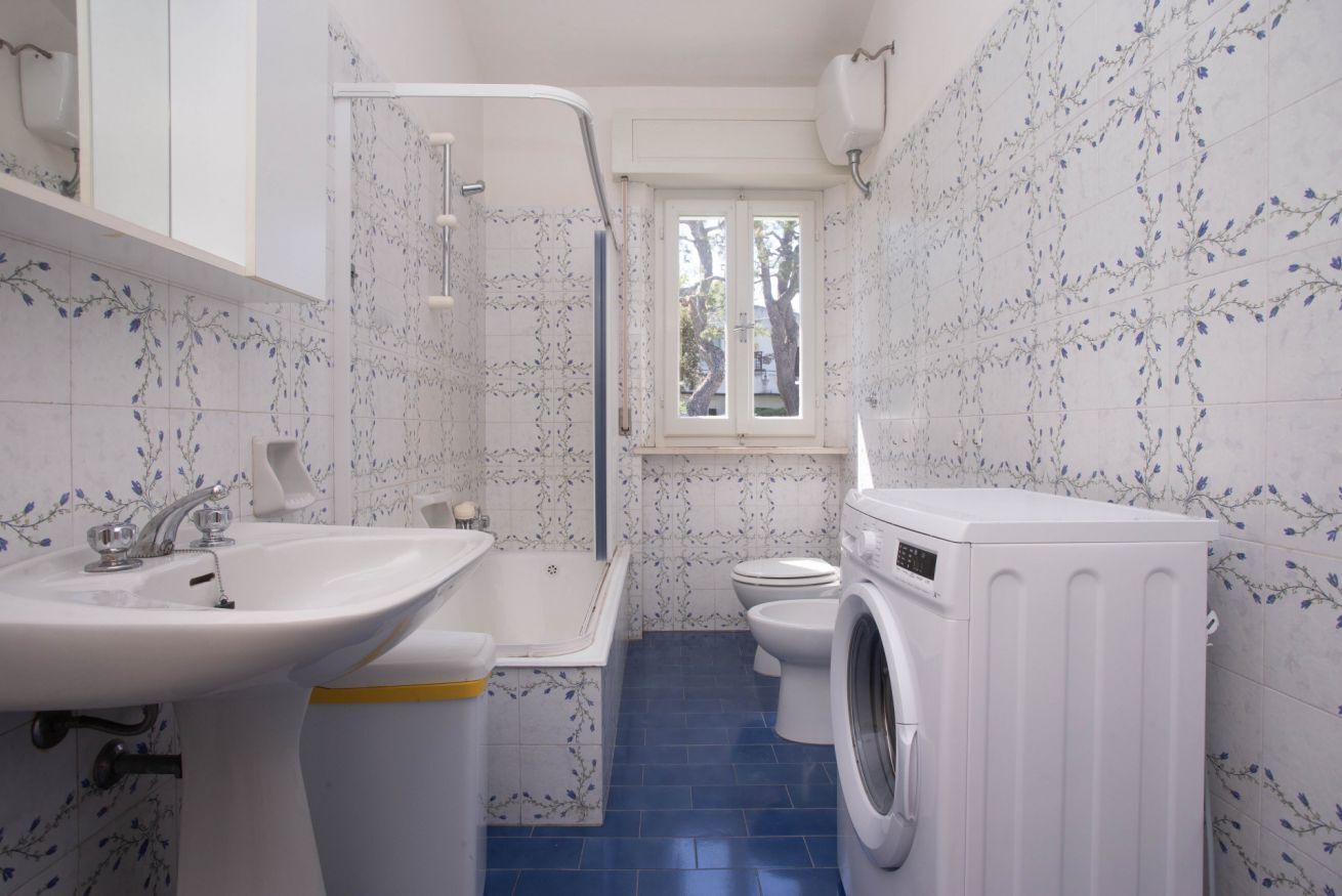 A compact bathroom with a sink, toilet, and washing machine, featuring blue-tiled flooring and floral wall tiles.