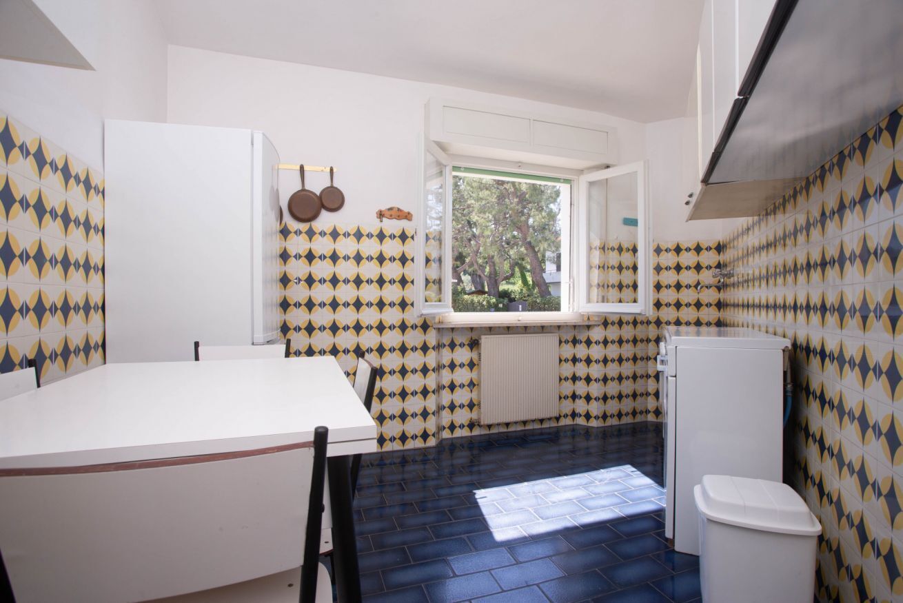 Una cucina compatta con una finestra, mobili bianchi e piastrelle decorative.