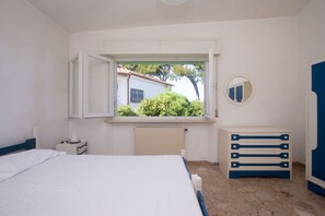 A bedroom with a bed, a dresser, a radiator, a window with an open shutter, and a mirror on the wall.