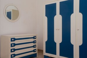 A room with a white dresser, a blue wardrobe, and a round mirror on the wall.