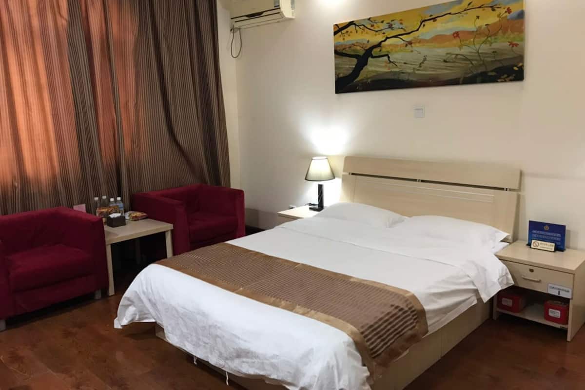 A hotel room with a bed, a desk, a chair, a lamp, and a painting on the wall.