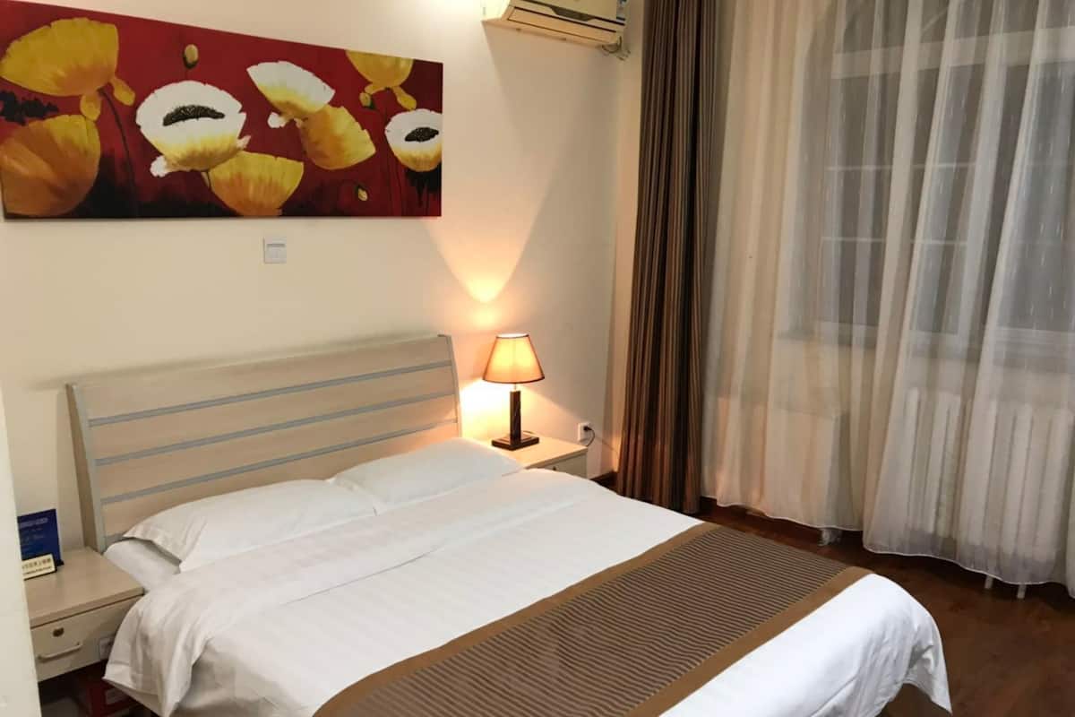 A hotel room with a bed, a nightstand, a lamp, a painting on the wall, and a window with curtains.