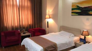 Habitación de hotel con dos camas, una silla roja, una mesita de noche con lámpara y un cuadro en la pared.