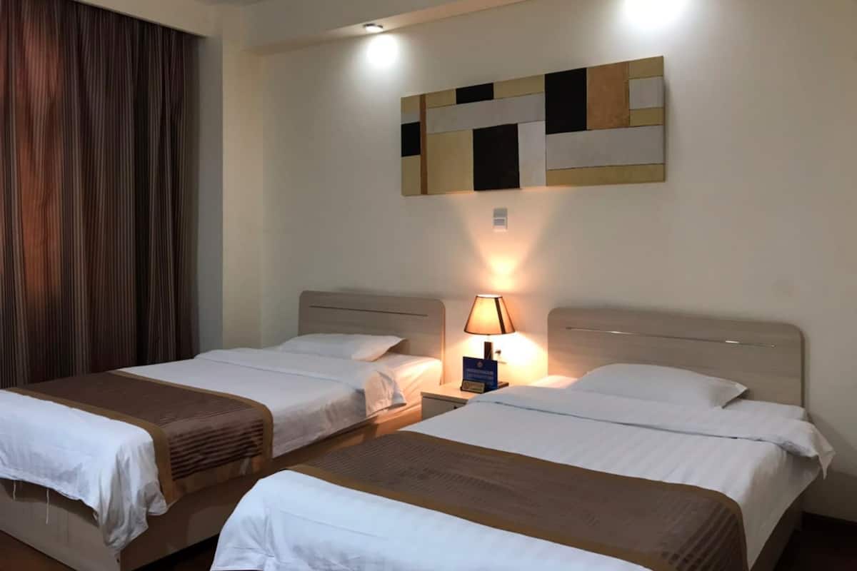 A hotel room with two beds, a nightstand, a lamp, and a wall-mounted artwork.