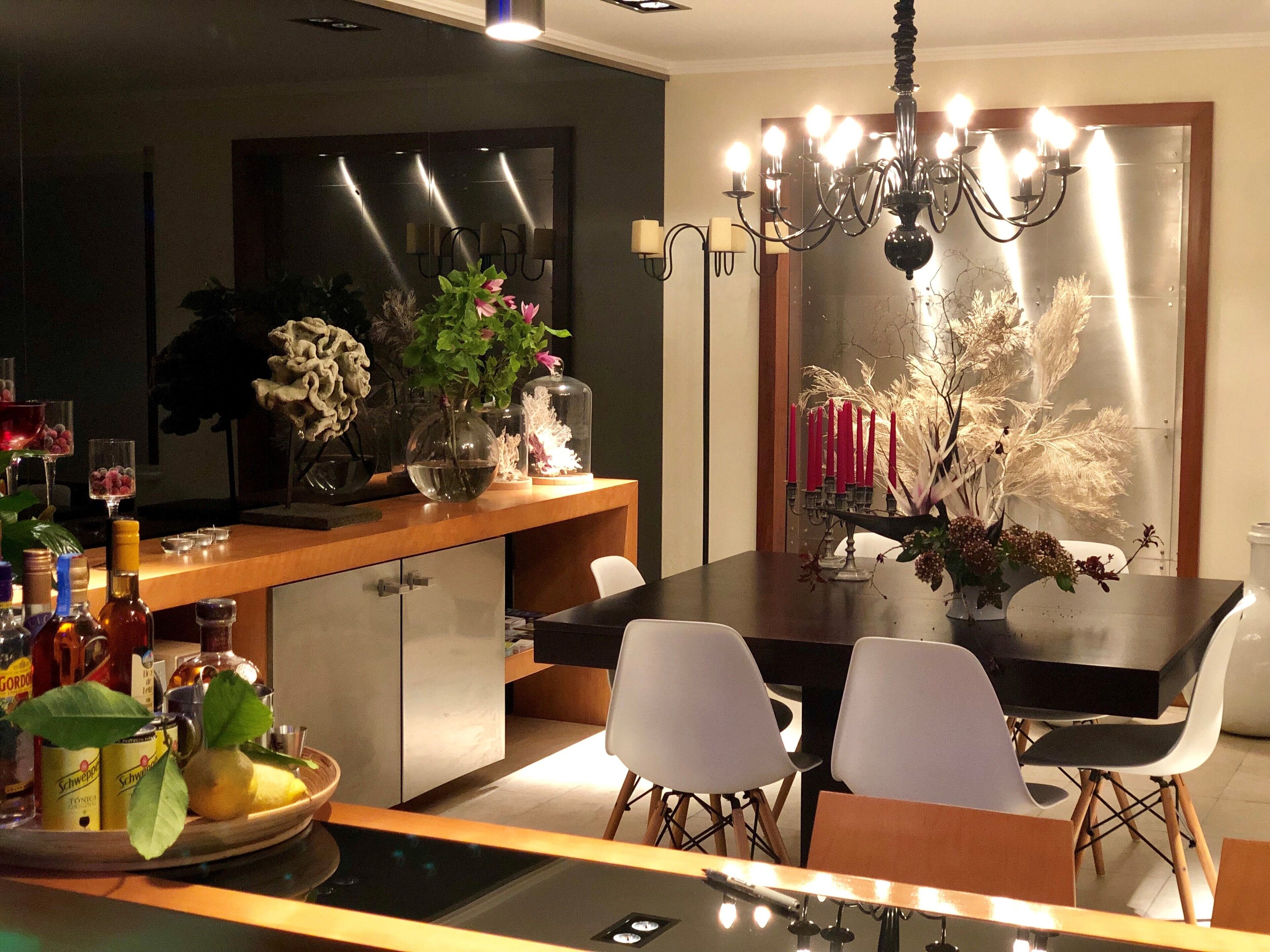 A modern dining area with a dark wooden table, white chairs, and a chandelier. There are various decorative items on the table, including flowers and candles.