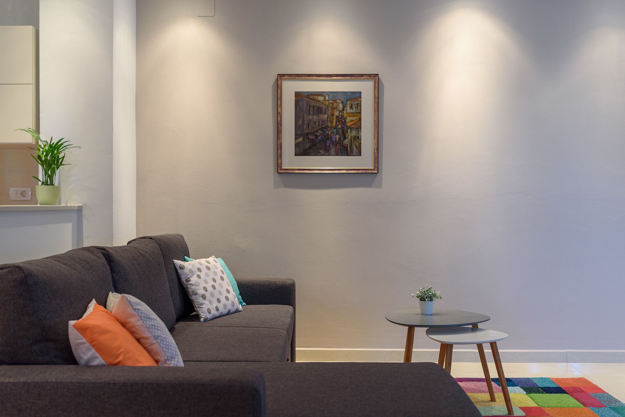 Un salon moderne avec un canapé gris, une petite table ronde et un tapis coloré.