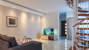 Een moderne woonkamer met een grijze bank, een flatscreen televisie en een trap.