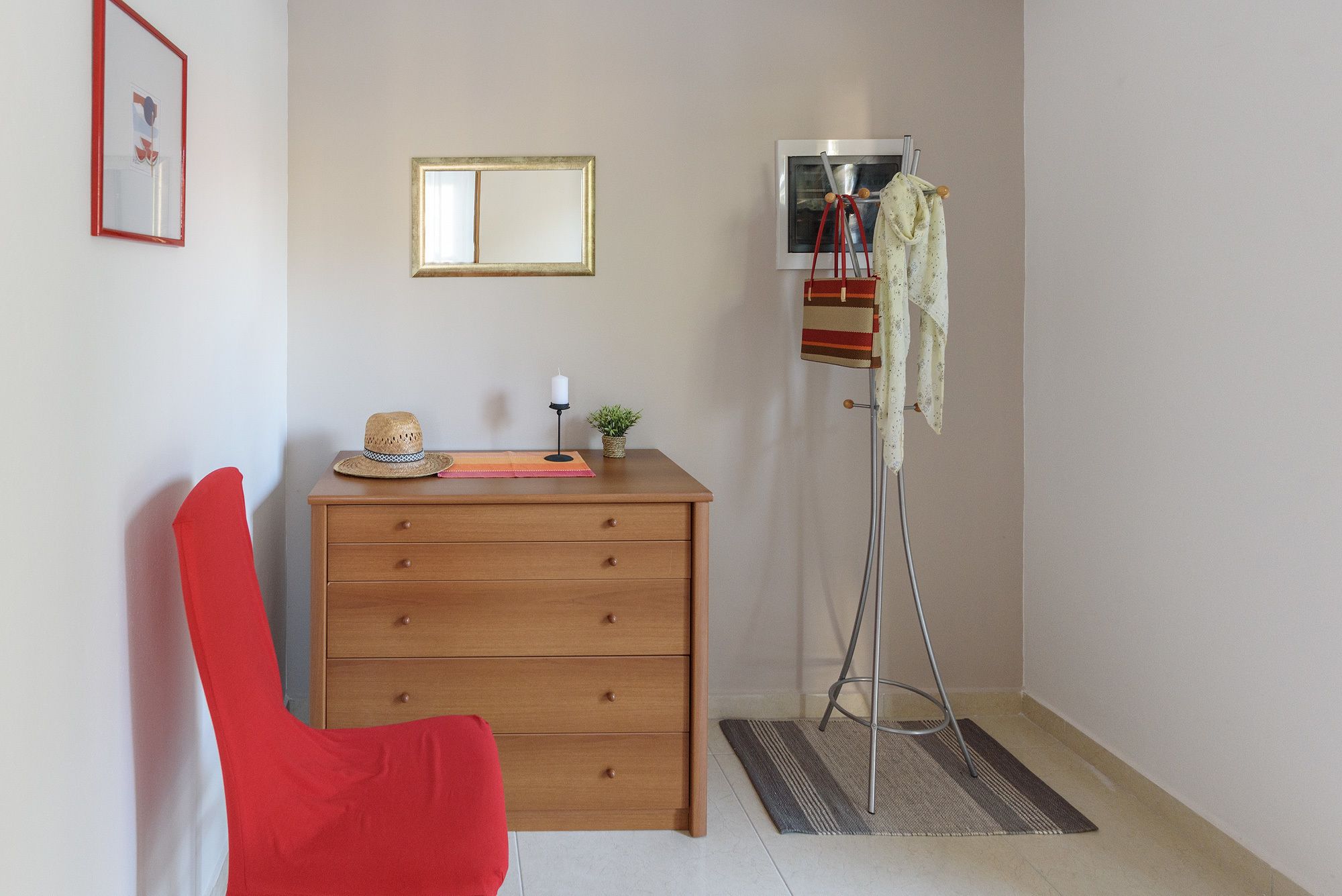 Une pièce comprenant une commode en bois, une chaise rouge, un lampadaire et un miroir accroché au mur.