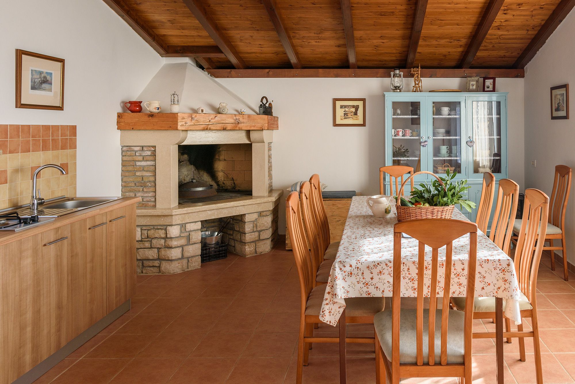 Une cuisine équipée d’un four à bois, d’une table à manger avec des chaises et d’un buffet avec des portes en verre.