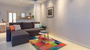 Een moderne woonkamer met een grijze modulaire bank, een klein rond tafeltje en een kleurrijk vloerkleed.