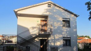 A two-story building with a balcony on the second floor, a stone wall in front, and a clear sky. - Apartment Razum A5 (Pula)