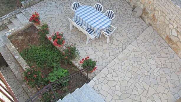 An outdoor patio with a stone floor, a white table with blue and white striped chairs, and red flowers in pots. - Apartment Razum A5 (Pula)