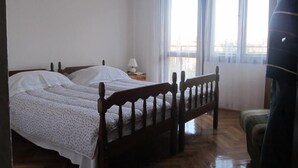 A bedroom with two wooden beds, a nightstand with a lamp, and a view of the outside through large windows. - Apartment Razum A5 (Pula)