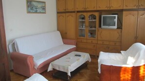 A living room with a sofa, armchairs, a small table, wooden cabinets, a television, and a painting on the wall. - Apartment Razum A5 (Pula)