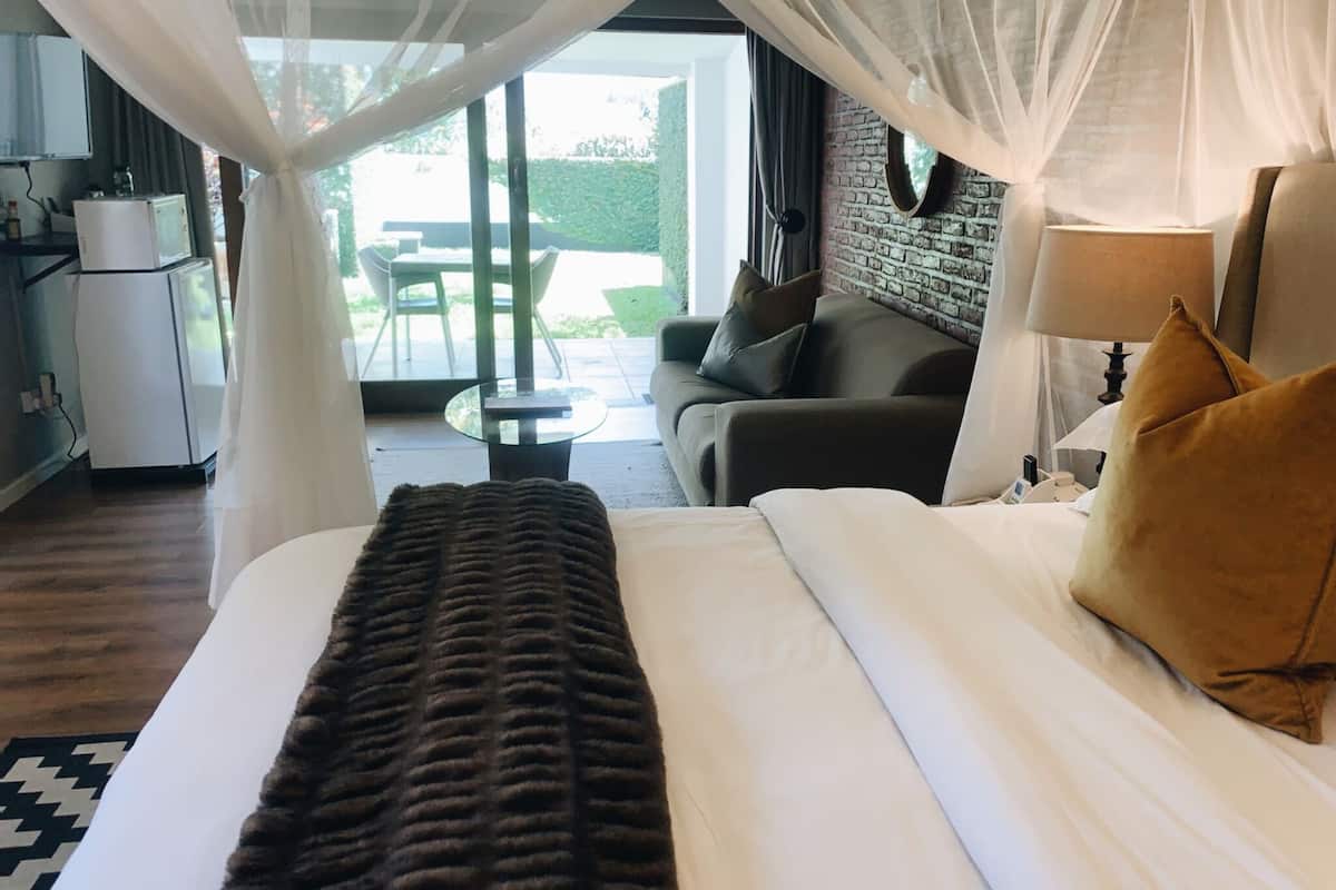 A hotel room with a bed, a sofa, a lamp, and a view of the outdoor area.