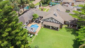 An aerial view of a residential area with a large house featuring a prominent swimming pool, a covered patio, and a well-maintained lawn. - The Leslie - Bed & Breakfast (Blantyre)