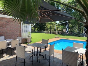 Zona junto a la piscina con pared de ladrillo, mobiliario exterior y una vista despejada del agua.