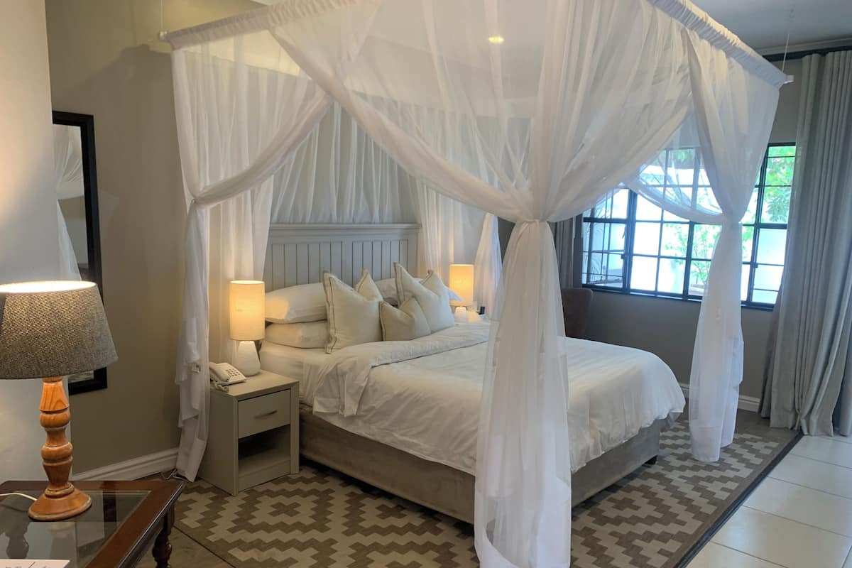 A bedroom with a four-poster canopy bed, bedside lamps, a nightstand, and a patterned rug.